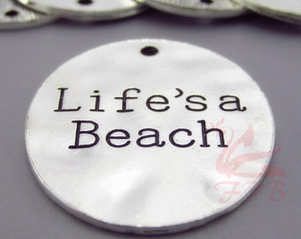 May include: A silver round charm with the text "Life's a Beach" in black lettering.