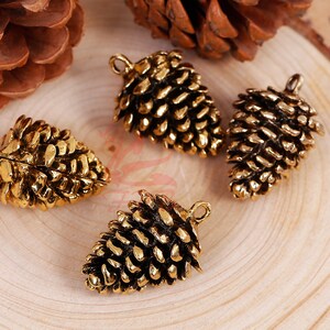 May include: Four gold-tone metal pine cone charms with a loop for hanging. The pine cones are detailed and realistic.