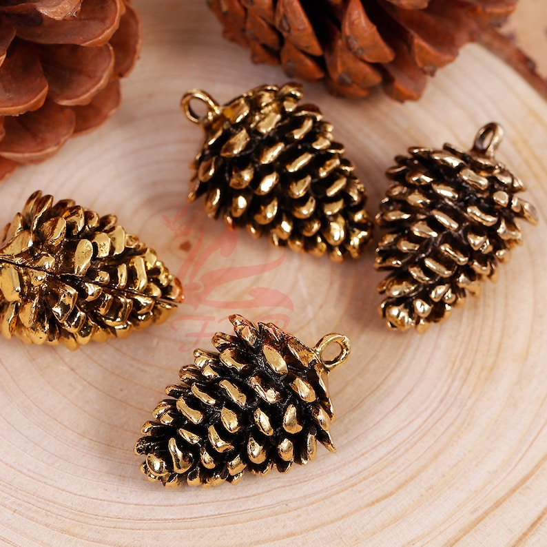 May include: Four gold-tone metal pine cone charms with a loop for hanging. The pine cones are detailed and realistic.