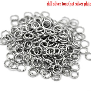 May include: A large pile of silver jump rings. The rings are small and round, and they are all the same size. They are made of a dull silver tone metal, not silver plated.