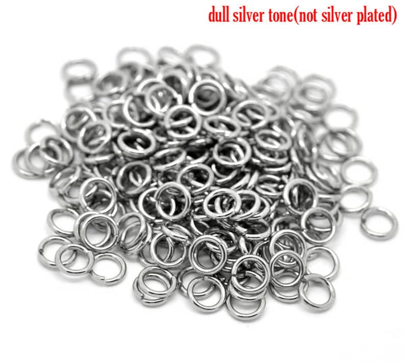 May include: A large pile of silver jump rings. The rings are small and round, and they are all the same size. They are made of a dull silver tone metal, not silver plated.