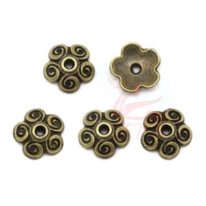 Może przedstawiać: Pięć antycznych, złotych metalowych nasadek na koraliki w kształcie kwiatu ze wzorem spiralnym.