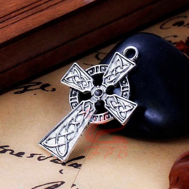 May include: A silver Celtic cross pendant with intricate knotwork designs. The cross is detailed with a circular border and a central knot.