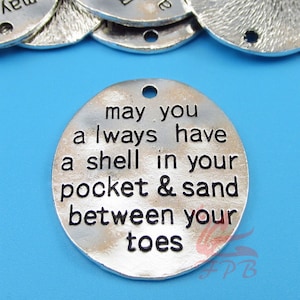 May include: Silver charm with the text "may you always have a shell in your pocket & sand between your toes".