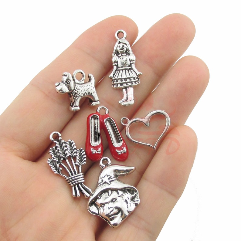Puede incluir: Un conjunto de dijes plateados con im&aacute;genes ic&oacute;nicas. Incluye un perro, una ni&ntilde;a, zapatos rojos, un coraz&oacute;n, un manojo de trigo y la cara de una bruja. Estos dijes son ideales para la creaci&oacute;n de joyas o proyectos de manualidades.