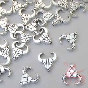 May include: A group of silver metal bull head charms with a geometric design. The charms have a hole at the top for attaching to jewelry or other crafts.