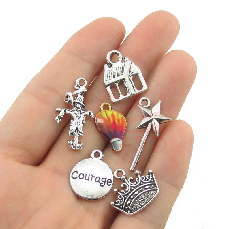 Puede incluir: Un conjunto de dijes plateados que incluyen una casa, un espantap&aacute;jaros, un globo aerost&aacute;tico, una varita de estrella, una corona y un dije circular con la palabra "Courage". Para bisuter&iacute;a o manualidades.