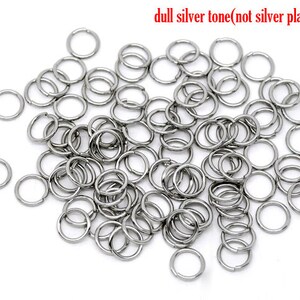 May include: A large pile of silver-toned jump rings. The rings are small and round, and they are all the same size. The rings are made of metal and have a dull finish.  The rings are not silver plated.