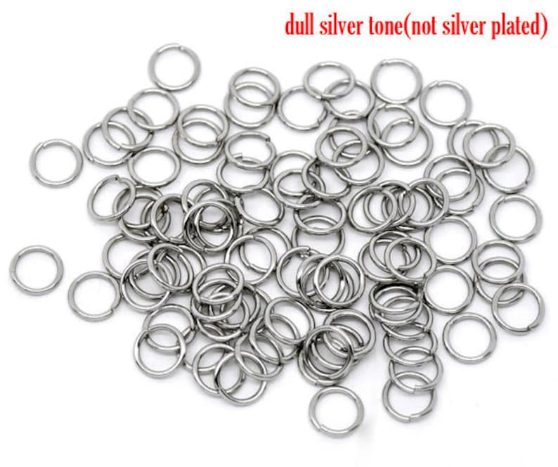 May include: A large pile of silver-toned jump rings. The rings are small and round, and they are all the same size. The rings are made of metal and have a dull finish.  The rings are not silver plated.