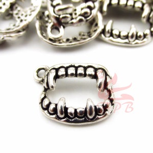 May include: Silver-toned metal charm shaped like a set of fangs. The charm has a loop at the top for attaching to a necklace or bracelet.