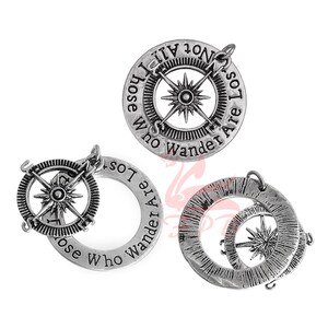 May include: Three silver-toned metal charms with compass designs and the inscription "Not all those who wander are lost".