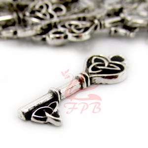 May include: A silver-colored key charm with a Celtic knot design on the head and the tip. The key has a detailed, vintage appearance. Other similar charms are visible in the background.
