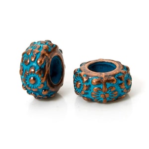 May include: Two turquoise and bronze-colored beads with floral patterns. The beads have a cylindrical shape with a large hole in the center. The bronze details are raised, creating a textured surface. The beads are on a white background.