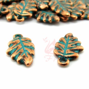 Op de afbeelding: Twee koperen bladeren met een turquoise groene emaille afwerking. De bedels hebben een lus aan de bovenkant om te bevestigen aan sieraden of andere knutselwerkjes.