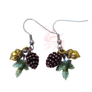 May include: A pair of dangle earrings featuring a nature-inspired design. Each earring has a silver hook, a small brown pinecone, a gold acorn, and a green leaf. The earrings are designed to resemble a miniature forest.