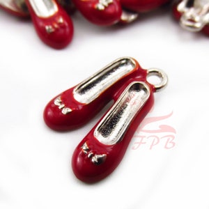 May include: A pair of red enamel shoe charms with silver accents and a bow detail. The charms have a loop for attaching to a bracelet or necklace.