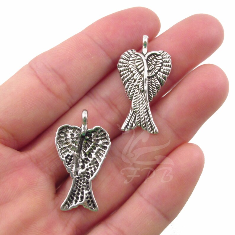 May include: Two silver angel wing charms with a detailed design. The wings are shaped like a heart and have a loop at the top for attaching to jewellery.