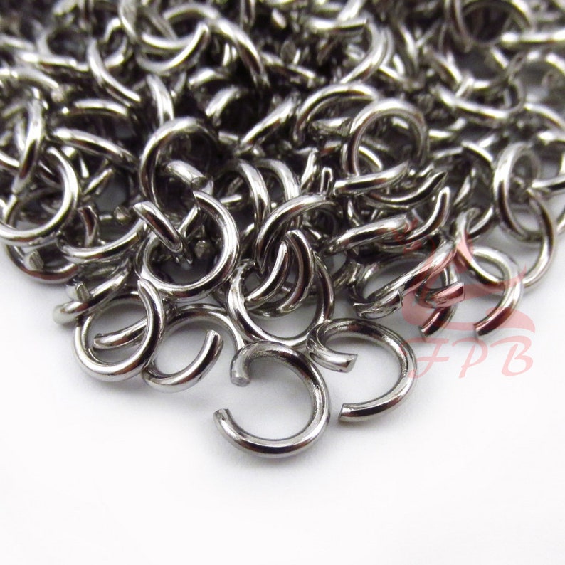 May include: A close-up of a pile of silver jump rings. The rings are small and have a smooth, polished finish.