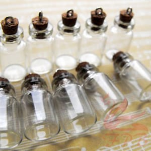 May include: A collection of ten clear glass bottles with cork stoppers and silver metal caps. The bottles are small and have a round shape. They are arranged in a row on a surface with a patterned design.