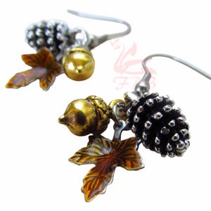 Puede incluir: Pendientes colgantes con abalorios con temática otoñal. Cada pendiente tiene un gancho plateado e incluye una piña, una bellota y un dije de hoja. Los dijes están detallados con tonos dorados, marrones y plateados, creando un accesorio inspirado en la naturaleza.