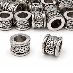 May include: A collection of cylindrical silver-toned metal beads featuring a textured surface and a raised triquetra knot design. Each bead has a smooth, raised rim at the top and bottom, with a hollow center for threading onto cords or jewelry wire.