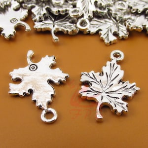 May include: Two silver-toned maple leaf charms with a loop at the top for hanging. The leaves have a detailed design and a slightly textured finish.