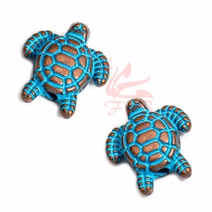 May include: Two turquoise blue turtle shaped beads with a copper finish. The beads have a detailed shell design.