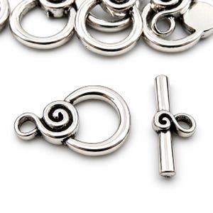 May include: A set of silver-toned metal toggle clasps for jewellery making. Each clasp consists of a circular ring with a spiral design and a matching T-bar component featuring a central spiral detail. The metal has a polished finish.