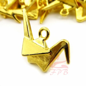 Op de afbeelding: Gouden origami kraanvogel bedel met een lus om te bevestigen aan sieraden of andere knutselwerkjes.