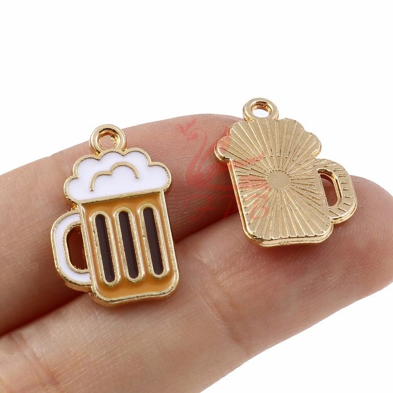May include: Two gold-colored metal charms shaped like beer mugs. One charm has a white foam top and brown stripes. The other charm has a sunburst design.