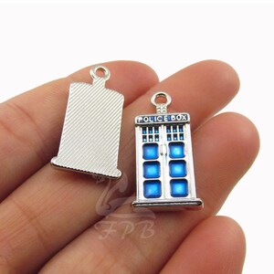 K&ouml;nnte beinhalten: Silberner Anh&auml;nger mit einem blauen und wei&szlig;en Emaille-Polizeikasten-Design. Der Anh&auml;nger tr&auml;gt die Aufschrift "Police Box" auf der Vorderseite. Die R&uuml;ckseite des Anh&auml;ngers ist schlicht silber.