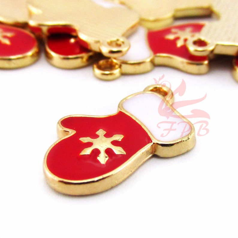 May include: Gold-tone metal Christmas mitten charm with red enamel and a white snowflake design. The charm has a loop for hanging.