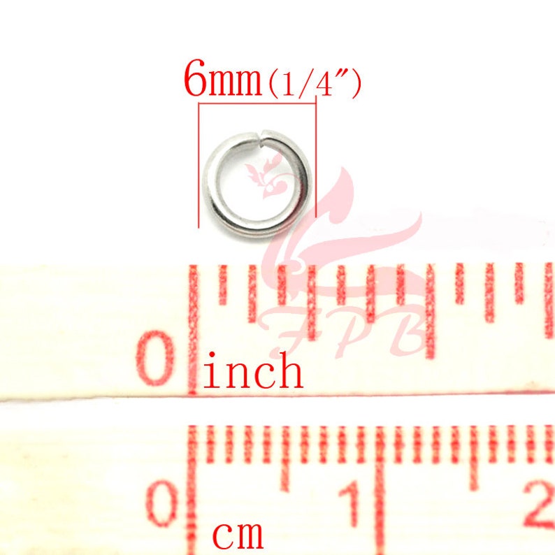 May include: A silver jump ring measuring 6mm (1/4 inch) in diameter. The ring is shown next to a ruler with inch and centimetre markings.