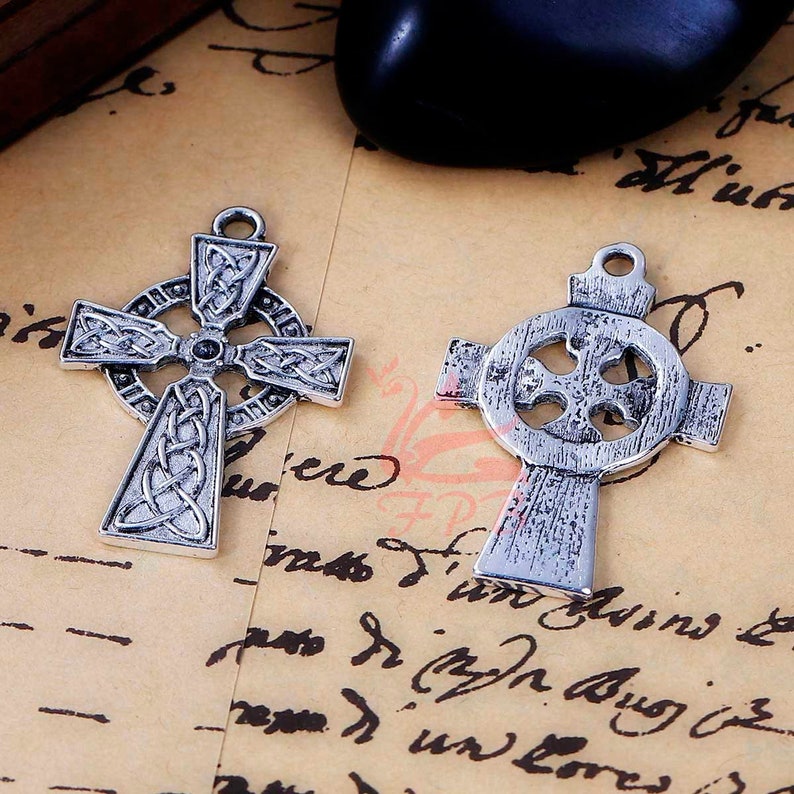 May include: Two silver Celtic cross charms with intricate designs. The crosses are both in a traditional Celtic style, with a circle in the center and a knotwork design around the edges. The charms are perfect for jewelry making or other craft projects.