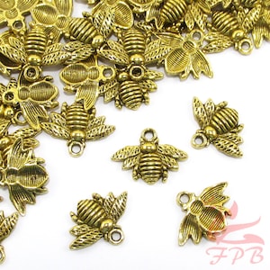 May include: A collection of gold-toned metal bee charms featuring intricate wings and a textured body. The charms have a loop at the top for attaching to jewellery or other crafts.