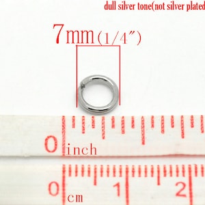 May include: A silver-toned metal jump ring measuring 7mm (1/4 inch) in diameter. The ring is shown next to a ruler for size reference.
