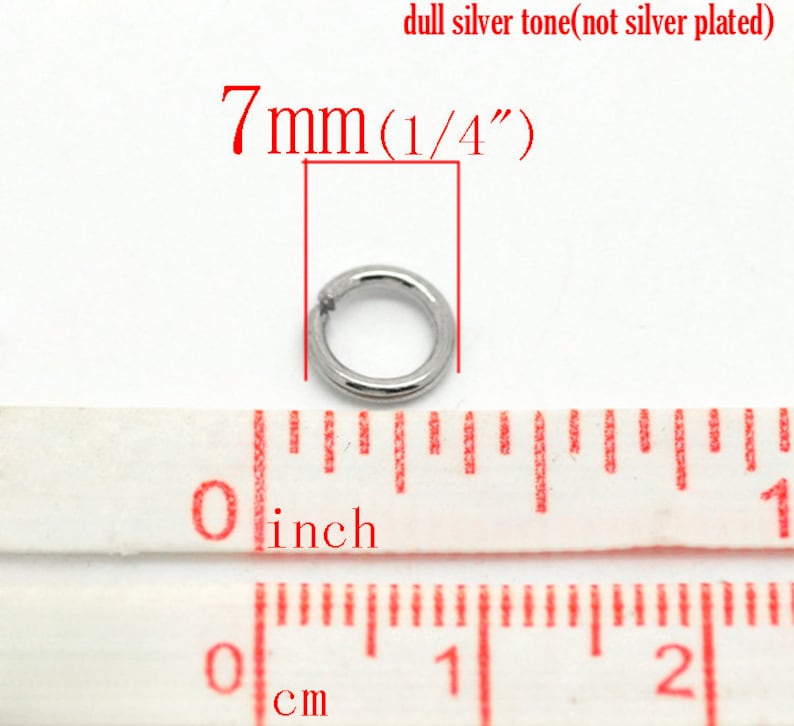 May include: A silver-toned metal jump ring measuring 7mm (1/4 inch) in diameter. The ring is shown next to a ruler for size reference.