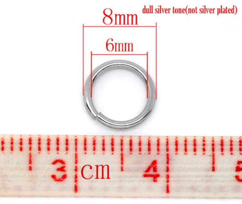 May include: A silver-toned metal jump ring measuring 8mm in diameter and 6mm in width. The ring is shown next to a ruler, with the measurement markings visible.