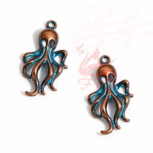 Könnte beinhalten: Zwei antike, kupferfarbene Kraken-Anhänger mit blauen Akzenten. Die Kraken-Anhänger haben ein detailliertes Design und sind perfekt für die Schmuckherstellung oder das Basteln.