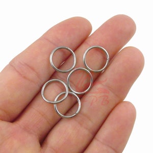 May include: Five silver metal key rings, also known as split rings, are shown in a hand. The rings are all the same size and are made of a smooth, shiny metal.