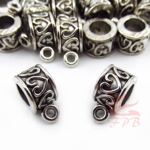 May include: A collection of silver-toned metal cylindrical beads featuring an embossed heart pattern around the exterior. Each bead includes a small circular loop attached to the side for hanging. The metal has a dark, oxidized finish.