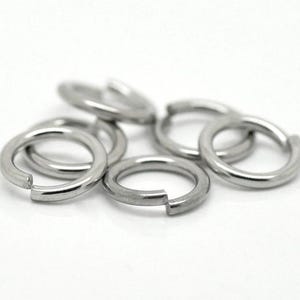 May include: A close-up of six silver jump rings. The rings are all the same size and are arranged in a loose pile.