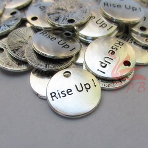 May include: A pile of silver-toned metal charms with the words "Rise Up!" engraved on them. The charms have a hole at the top for attaching to a necklace or bracelet.