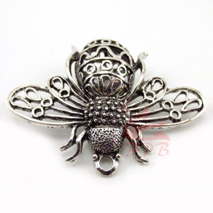 May include: Silver-toned metal bee charm with intricate filigree wings and a detailed body. The bee has a loop at the bottom for attaching to jewelry or crafts.
