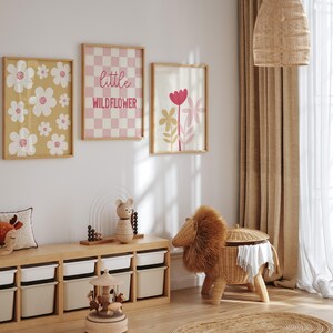May include: Three framed prints with a floral theme. The prints feature pink and white flowers on a yellow background, a pink and white checkered pattern with the text "little wildflower", and pink and white flowers on a white background.