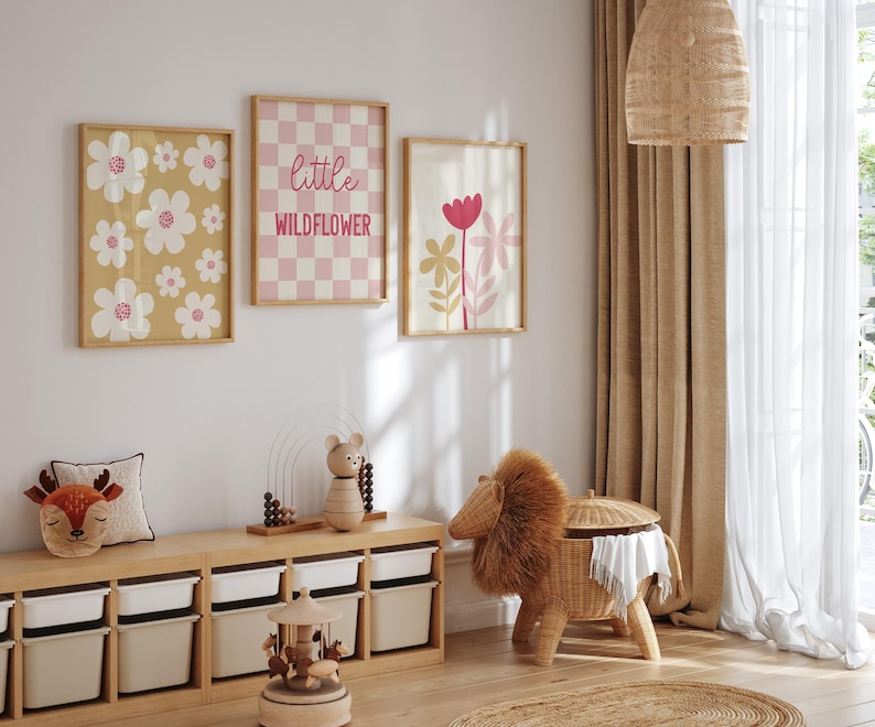 May include: Three framed prints with a floral theme. The prints feature pink and white flowers on a yellow background, a pink and white checkered pattern with the text "little wildflower", and pink and white flowers on a white background.