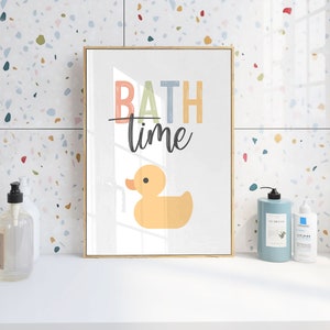 May include: A framed print with the text "BATH time" in colorful letters and a yellow rubber duck illustration. The print is hanging on a white tiled wall with a terrazzo pattern.
