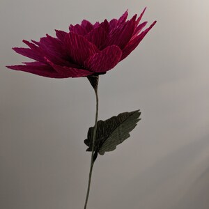 May include: A single, large, magenta paper flower with a green paper leaf on a stem.