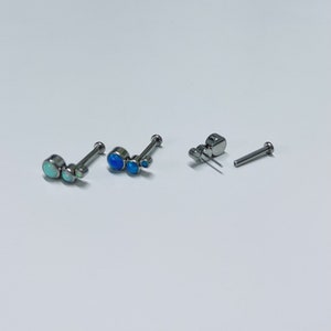 May include: Two sets of nose rings with three opal stones each. One set has blue opals and the other has white opals. The rings are made of stainless steel.
