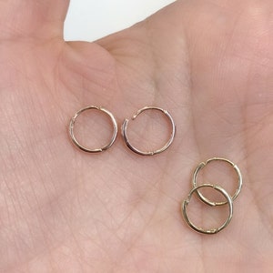 May include: Three pairs of gold hoop earrings. The earrings are different sizes. The earrings are on a hand.